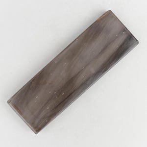 Könnte beinhalten: Eine rechteckige Platte aus poliertem versteinertem Holz mit einer glatten Oberfläche und einer natürlichen Maserung in Dunkelbraun, Grau und Beige, die feine weiße Mineraleinschlüsse im dichten, steinartigen Material aufweist.