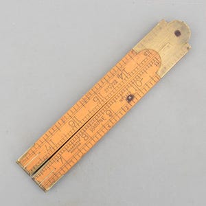 May include: A vintage folding ruler made of wood and brass. The ruler is orange with black markings and brass end pieces. The ruler is marked with the text "RABONE" and "MADE IN ENGLAND". The ruler measures up to 45.7 cm.