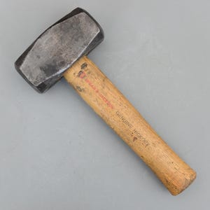 May include: A heavy-duty sledgehammer with a dark, rectangular head and a wooden handle. The handle is made of genuine hickory and features the brand name "SPEAR & JACKSON" in red lettering.