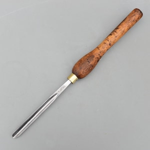 May include: A wood turning gouge with a wooden handle and a metal blade. The handle is a dark brown color with a brass ferrule. The blade is silver and has a curved shape. The tool is designed for woodworking.