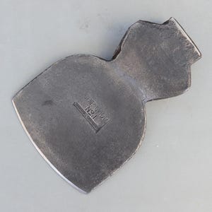 Puede incluir: Una cabeza de hacha de metal gris oscuro con una hoja ancha y curva y un talón cónico. La superficie presenta el texto en relieve "CHIP CHOP" sobre "No 11" y un texto más pequeño parcialmente oscurecido debajo del número, centrado en la cara.