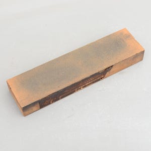 Peut inclure: Une pierre à aiguiser rectangulaire brune avec une étiquette noire qui indique "Norton ABRASIVE"