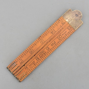 May include: An antique wooden folding ruler with brass fittings. The ruler is orange with black markings and numbers. The ruler is marked with the text "Made in England" and "Warranted Boxwood". The ruler is approximately 17 inches long when fully extended.