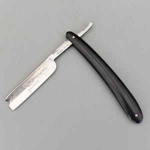 May include: A vintage straight razor with a black handle and a silver blade. The blade is marked with the words "CROWN & SWORD" and "MAGNETIC". The razor is open and on a grey background.