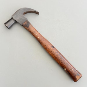 May include: A vintage hammer with a wooden handle. The hammer head is made of metal and has a claw.