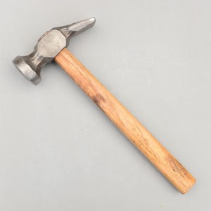 May include: A metal hammer with a wooden handle. The hammerhead is silver and has a flat face on one side and a curved, pointed end on the other. The handle is made of light brown wood.