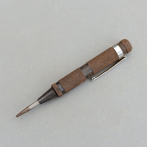 May include: A rusty metal centre punch with a silver metal cap and a retractable handle. The tool is used for marking metal.