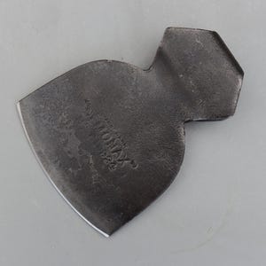 以下が含まれることがあります： カーブした刃と質感のある表面を持つ、ヴィンテージの濃いグレーの金属製手斧の頭。表面には「DEMONAX」と「1924」の文字が刻印されています。手斧の頭には六角形の柄があります。