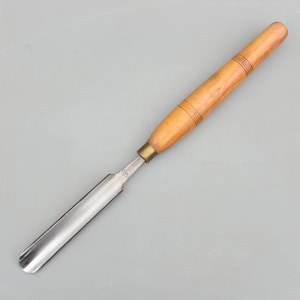 May include: A woodturning gouge featuring a curved steel blade and a cylindrical light brown wooden handle. The tool includes a brass ferrule connecting the metal shaft to the wood, with three decorative rings etched into the handle surface.