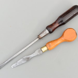 May include: Two screwdrivers with different handles. One has a dark brown wooden handle and the other has an orange plastic handle.