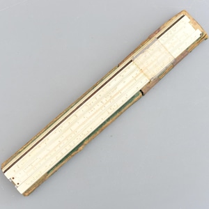May include: A vintage slide rule with a cream-colored scale and a brown and green leather case. The slide rule features multiple scales and markings, and the case shows signs of wear.