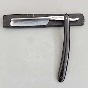 以下が含まれることがあります： 黒い持ち手と「But First, Coffee」の文字が黒い手書き風フォントで書かれた白いセラミックマグ。マグカップは白い表面に置かれています。