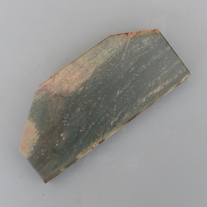 Puede incluir: Una piedra de forma irregular con una textura rugosa, que presenta tonos de verde, gris y marrón.