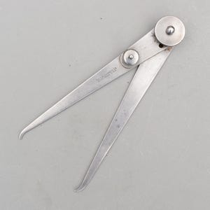 Puede incluir: Una herramienta de calibre exterior plateada vintage. La herramienta tiene dos patas curvas conectadas por un pivote y un pequeño tornillo de ajuste. El texto "The L.S. Starrett Co. Athol Mass. U.S.A." está estampado en una pata.