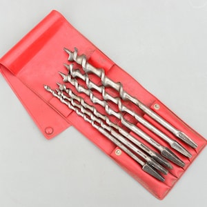 Könnte beinhalten: Ein Satz von sechs silbernen Forstnerbohrern in verschiedenen Größen, präsentiert in einer roten Vinyltasche. Die Bohrer haben ein Spiraldesign und sind für die Holzbearbeitung konzipiert. Die Tasche ist geöffnet und zeigt die Werkzeuge.