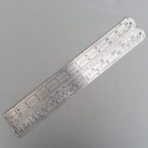 Puede incluir: Una regla plegable de plata con marcas en pulgadas y fracciones de pulgada. La regla está marcada con números del 1 al 12.