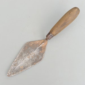 May include: A vintage, rusty, metal trowel with a wooden handle. The trowel has a diamond-shaped blade and is used for spreading mortar.