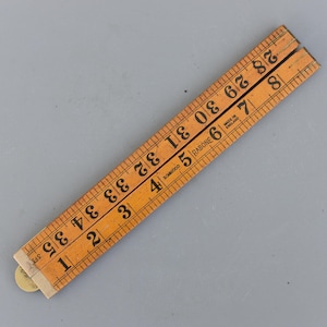 Puede incluir: Una regla plegable de madera vintage, marcada con números negros y líneas de medición. La regla Rabone mide hasta 88,9 cm y está marcada con "Made in England". La regla es de color marrón claro.