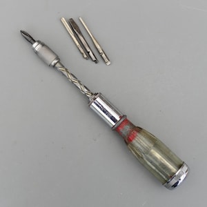 May include: A vintage screwdriver set with a clear, ribbed handle and a silver metal shaft. The set includes a Phillips head bit and several flathead bits. The handle has red paint near the base.