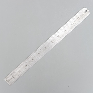 Peut inclure: Une règle en métal argenté avec des marquages en centimètres de 1 à 30. La règle a un trou à l'extrémité et repose sur une surface grise. Le mot "LONDON" est imprimé sur la règle.