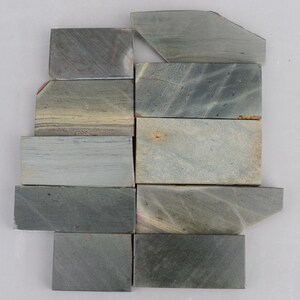 May include: A set of ten green and grey sharpening stones, arranged in a staggered pattern. The stones are rectangular and have a rough, textured surface.