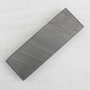 Può includere: Una pietra per affilare rettangolare grigia con una superficie testurizzata.