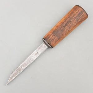 May include: A vintage knife with a wooden handle and a metal blade. The handle is a warm brown color, and the blade is silver. The text "T. SKAV" is visible on the blade. The knife is designed for cutting.