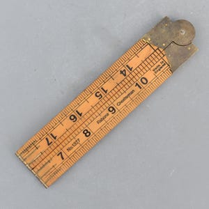 May include: A vintage wooden folding ruler with brass fittings. The ruler is marked with inch measurements and the numbers 7 through 17 are visible. The text "Rabone Chesterman" and "Made in England" are also visible.