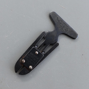 Puede incluir: Una herramienta de metal oscuro con un mango en forma de T y un mecanismo similar a unas tijeras. La herramienta tiene el texto "BRITISH KUTTNER PATENT" y otro texto. La herramienta está sobre una superficie gris.