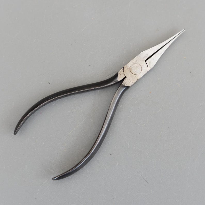 May include: Needle-nose pliers with a silver head and black handles. The pliers have long, tapered jaws for precision work. The handles are curved for a comfortable grip. The tool is designed for gripping, bending, and cutting small objects.