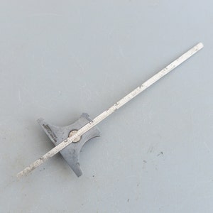 May include: A silver metal protractor with a ruler attached. The ruler is marked in inches.