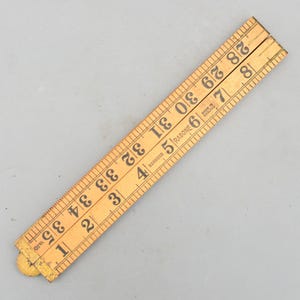 May include: A vintage wooden folding ruler, marked with black numerals and inch measurements from 1 to 35. The ruler is made of boxwood and has the text "RABONE" and "MADE IN ENGLAND" printed on it. Approximately 89 cm in length.
