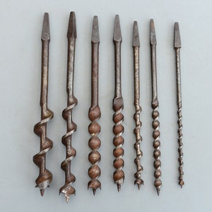 Może przedstawiać: Zestaw ośmiu antycznych wierteł ze spiralnym wzorem. Wiertła są wykonane z metalu i mają brązową patynę.