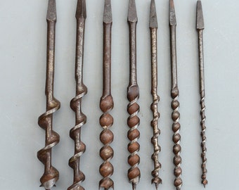 May include: A set of eight antique drill bits with a twisted, spiral design. The drill bits are made of metal and have a brown patina.