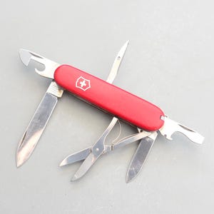 May include: A red Swiss Army knife with a variety of tools, including a blade, a bottle opener, a screwdriver, and a pair of scissors.