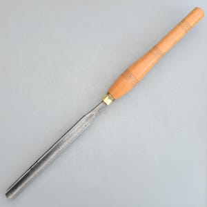 Op de afbeelding: Een houtsnijgereedschap met een lange, dunne metalen mes en een houten handvat.