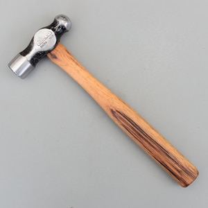 May include: A ball-pein hammer with a wooden handle. The hammer head is silver and black, with the brand name "STANLEY" visible. The handle is made of light brown wood.