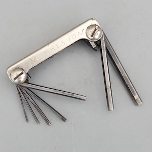 May include: A vintage folding hex key set with a silver-toned metal handle stamped with the word PRESTON. The tool features multiple dark grey steel hexagonal keys of varying sizes that pivot from the central handle, secured by two flat-head screws.
