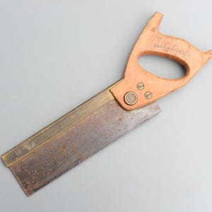 Può includere: Una sega a mano vintage con una lama in ottone e un manico in legno. Il manico ha un pomo in ottone e il testo "Spear & Jackson" è stampato su di esso.