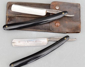 May include: Two vintage straight razors with black handles and silver blades. The razors are in a brown leather case with brass snaps. The blades are inscribed with "Hollow Ground Razor Fully Warranted" and "Gordon Armstrong Razor Fully Warranted Sheffield".