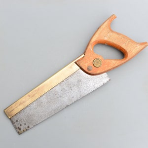 May include: A vintage hand saw with a brass blade and a wooden handle. The handle is a light brown colour and has a brass knob.