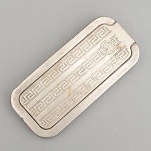 Peut inclure: Un étui de rasoir en métal argenté avec un motif de clé grecque et un petit emblème d'une personne assise sur une chaise.