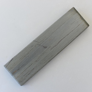 May include: A rectangular sharpening stone with a grey, textured surface. The stone has visible grain-like patterns and is designed for sharpening knives and tools. The stone is approximately 15 cm long.