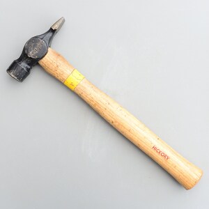 May include: A black and yellow hammer with a wooden hickory handle. The hammer has a yellow stripe on the handle and the word "HICKORY" is printed in red on the handle.