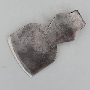 May include: A weathered axe head with a metallic finish. The axe head features a curved blade and a textured surface, with the text "MORRIS DEVON" in red. This tool is likely for woodworking or similar tasks, showing signs of age and use.