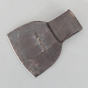 May include: A vintage metal tool with a wide, curved blade and a rectangular handle. The blade has a sharp edge and the text "THE WIZARD" is stamped on the surface. The tool has a dark, aged appearance.