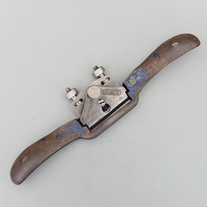 May include: A vintage metal spokeshave tool with a curved blade and wooden handles. The tool has a silver-colored blade and adjustment knobs, with some blue paint visible on the handles. The tool is marked "RECORD" and "NO 0161".