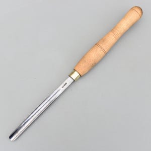 Puede incluir: Una gubia para trabajar la madera con una hoja curva de acero pulido y un mango de madera clara. El mango tiene un extremo redondeado y está asegurado con una férula de latón. La herramienta está diseñada para dar forma y tallar madera.