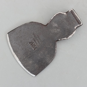 May include: A vintage axe head with a dark, weathered appearance. The metal tool features a curved blade with a white edge and a textured handle socket. The word "FORCE" is stamped on the axe head, along with other text.