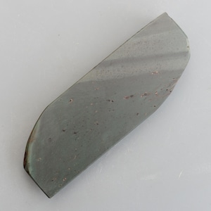 May include: A dark green sharpening stone with a slightly curved shape and a rough, textured surface.